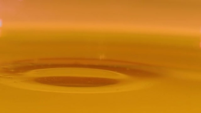 宏观: 金色的水滴落入装满冷榨橄榄油的容器中。