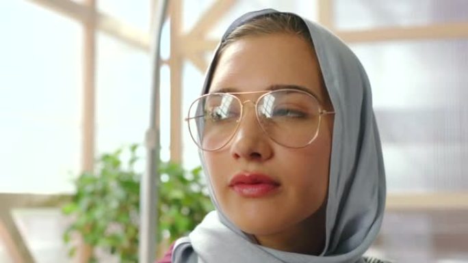 头巾，穆斯林妇女，在家里以和平与平静的心态思考咖啡或伊斯兰茶。来自以色列的年轻女性放松地看着窗外，带