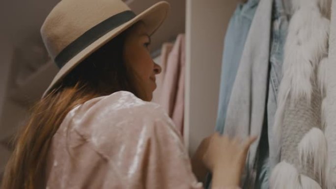 年轻女子戴着帽子，从衣柜里挑选衣服