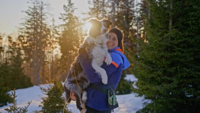 一名年轻女子在日出时抱着她的狗在雪坡上的SLO MO肖像照片