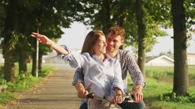 年轻无忧无虑的幸福情侣的真实照片在一个阳光明媚的日子里，他们很开心，喜欢一起在绿色公园骑自行车。