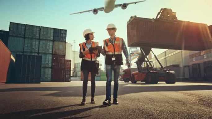 带平板电脑的女工业工程师和戴着安全帽的男工头工人在集装箱码头行走。VFX飞机在天空中飞行，双梁龙门起