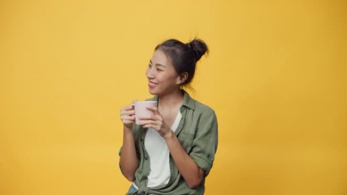 亚洲青年女士拿着一杯茶或咖啡站在孤立的黄色空白空间背景看着相机感到新鲜和梦幻放松给标志展示广告微笑兴