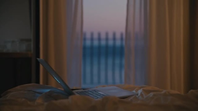 笔记本电脑站在酒店房间的床上，晚上可以看到大海