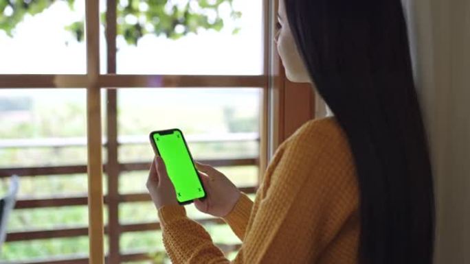 女士，一头黑发的年轻女子在家中使用带有色度键绿屏的智能手机