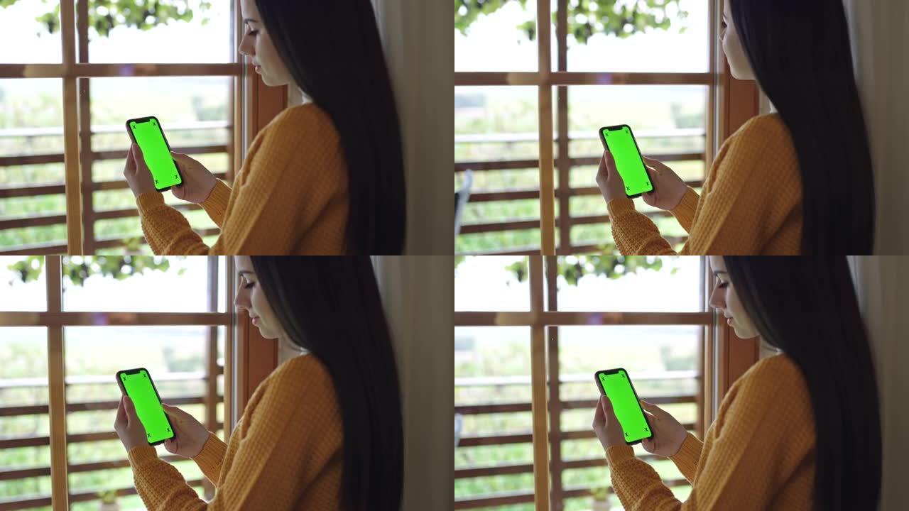 女士，一头黑发的年轻女子在家中使用带有色度键绿屏的智能手机
