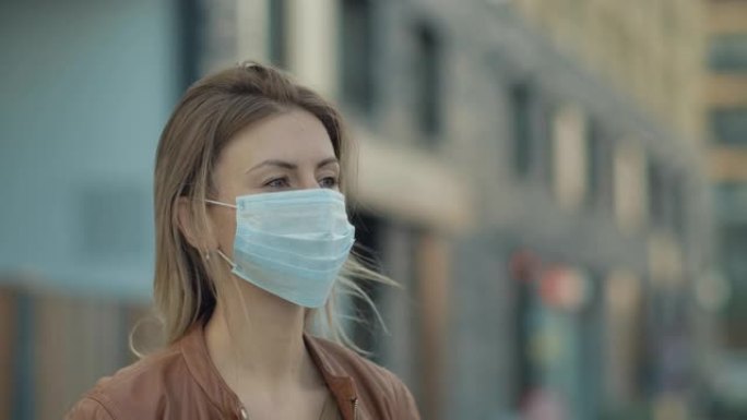 现代金发年轻一名戴着防护医用口罩的女子的特写肖像。安全概念。在检疫中关注社交距离的人。城市慢动作4k