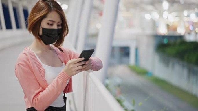 亚洲孤独女子戴着防护口罩，在商店使用智能手机