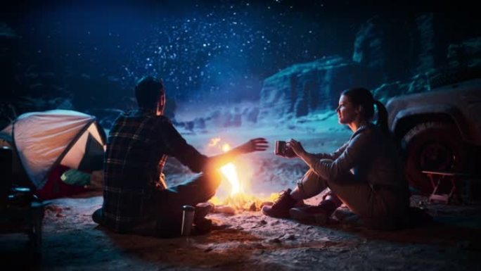 快乐情侣大自然一起在峡谷露营，坐在篝火旁分享一杯饮料，夜空观赏。两个旅行的人聊天，计划旅行，看看银河