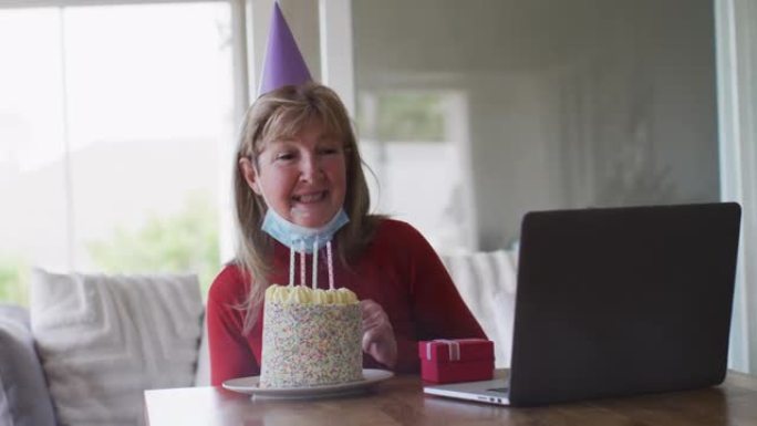 高级妇女在家在笔记本电脑上进行视频聊天时吹蛋糕