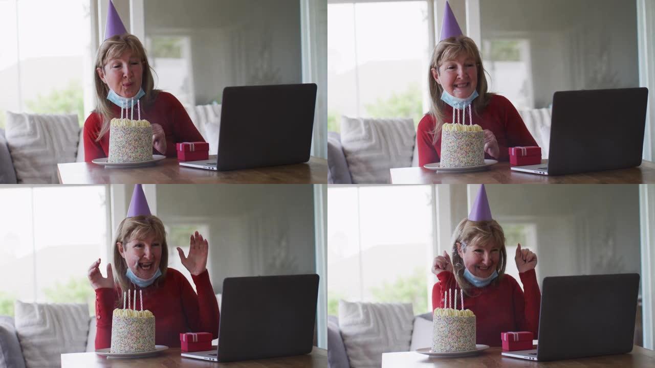 高级妇女在家在笔记本电脑上进行视频聊天时吹蛋糕