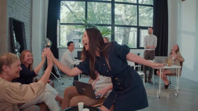 职业成功年轻的亚洲女商人进入办公室跳舞庆祝成就受到团队慢动作的欢迎。