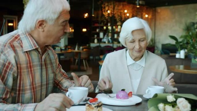 幸福的高级夫妇在餐厅吃着蛋糕喝茶聊天的肖像
