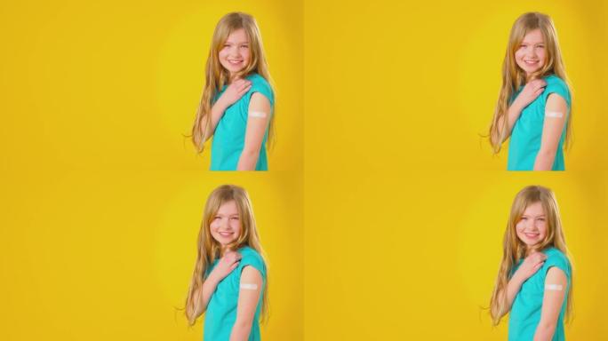 工作室拍摄的微笑女孩，手臂上贴石膏看着黄色工作室背景下的相机-慢动作拍摄