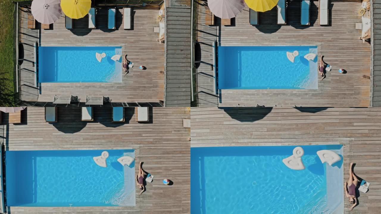 空中年轻女子在游泳池边缘的露台上放松