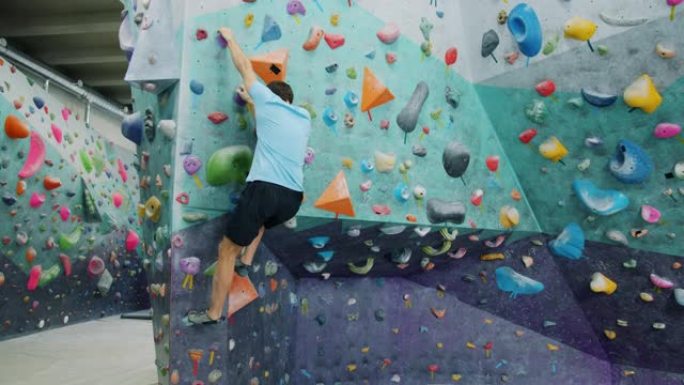 室内攀岩馆里的运动男训练拿着人造岩石爬上墙