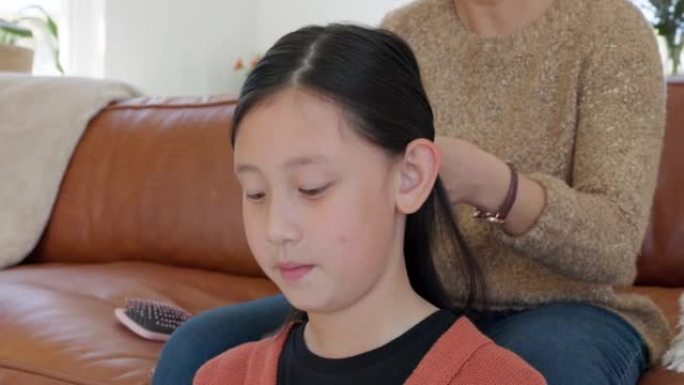 亚洲儿童、家庭发辫和沙发上的母亲在客厅进行头发护理、粘合和发型。妈妈沙发，小女儿和美发师与妈妈女孩在