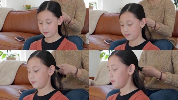 亚洲儿童、家庭发辫和沙发上的母亲在客厅进行头发护理、粘合和发型。妈妈沙发，小女儿和美发师与妈妈女孩在