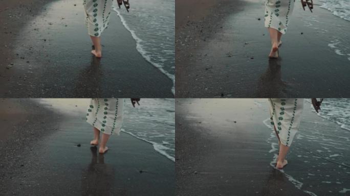 度假时，穿着裙子的快乐旅游女人的后视脚赤脚沿着热带沙滩在海浪边缘行走
