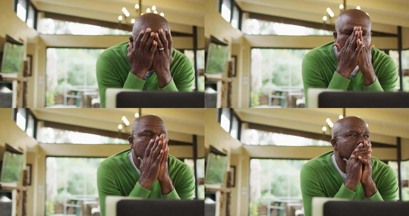 疲惫的非洲裔美国高级男子在厨房工作，使用笔记本电脑和摩擦眼睛