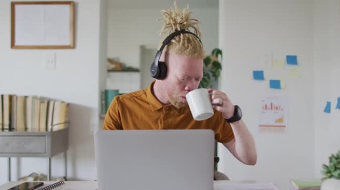 白化病非裔美国男子，长发lock喝咖啡，在笔记本电脑上进行视频通话