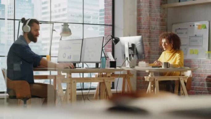 两名经理坐在大窗户旁边的桌子后面，可以看到城市景观，并在计算机上处理营销活动报告。在创意办公室从事项