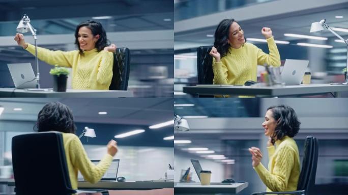 360学位办公室: 微笑的西班牙裔女商人坐在办公桌前在电脑上工作，一边听音乐一边跳舞。拉丁女企业家快