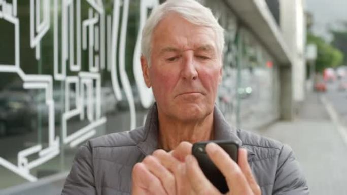 老人独自站在镇上时，用电话打字并在线发送短信。开朗无忧无虑的退休男性在城市中搜索互联网。成熟的家伙滚