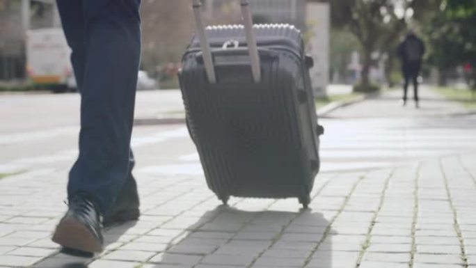 男性公司高管拉着行李箱，步行到城市机场航站楼出差的特写镜头。正式的企业家带着行李过马路前往酒店或家中
