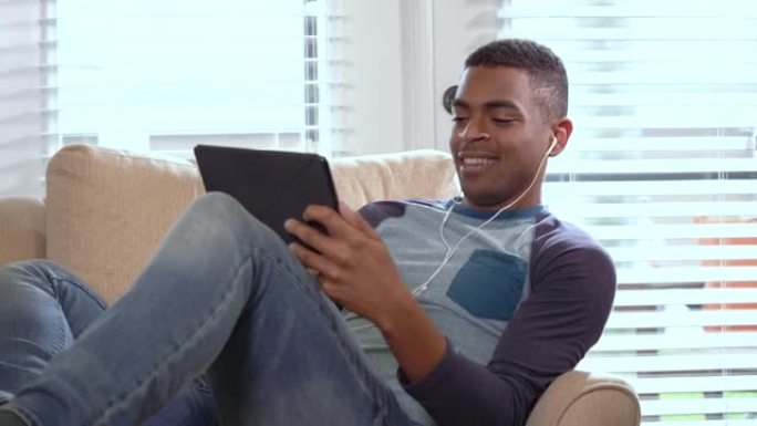 坐在扶手椅上的年轻非裔美国人，平板电脑，耳塞