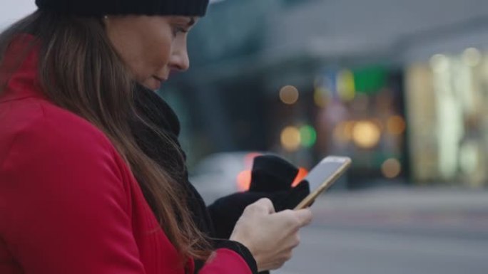 穿着红色外套的女士在城市的人行道上使用智能手机