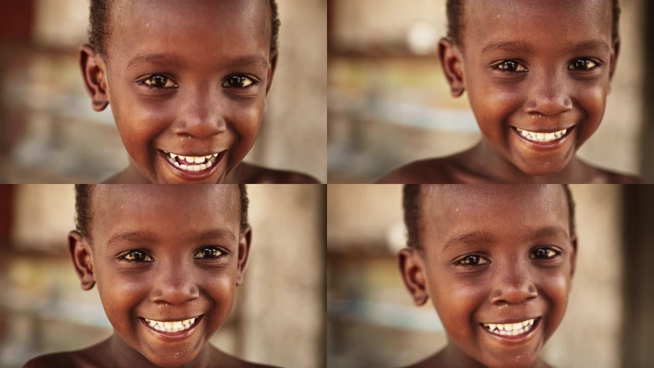 一个害羞的地道的非洲男孩在模糊的背景下对着镜头微笑和大笑的特写肖像。代表未来、希望和接受的黑人男性孩