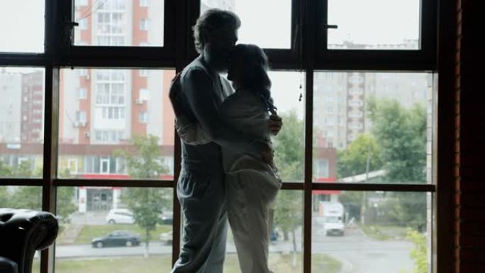 站在全景窗户背景下的男人和女人拥抱表达爱的剪影