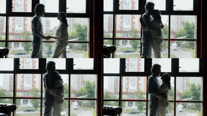 站在全景窗户背景下的男人和女人拥抱表达爱的剪影