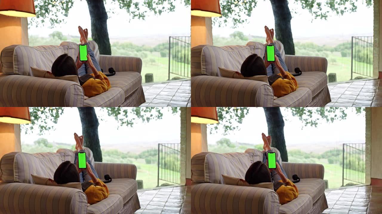 DS年轻女子躺在露台上的沙发上，使用带色度键绿屏的智能手机