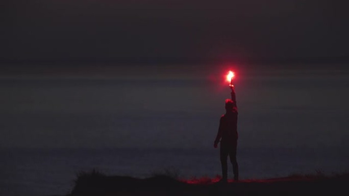 这个人站在海边，手里拿着一根火棍