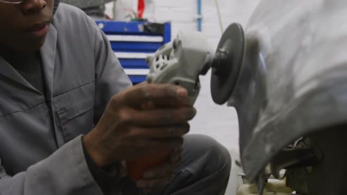 非裔美国男性汽车修理工在汽车侧面使用角磨机