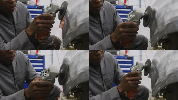 非裔美国男性汽车修理工在汽车侧面使用角磨机