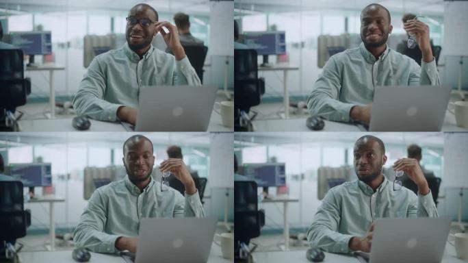 现代办公室: 快乐的黑色IT程序员在笔记本电脑上工作的肖像，与同事交谈，集思广益。戴眼镜的男软件工程