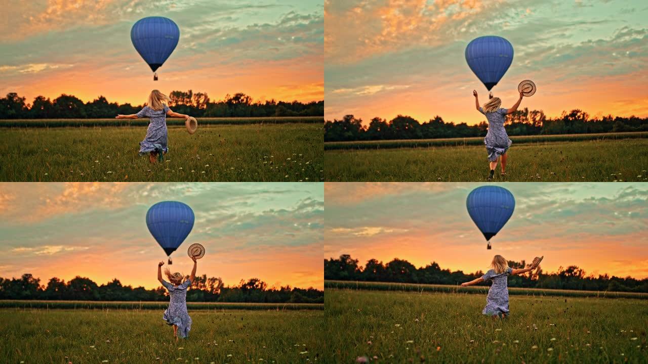 超级慢动作女人在日落时分穿过草地奔向飞行的热气球