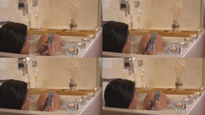 特写: 浸泡在浴缸里时用手机拍摄的年轻女士的后视镜头