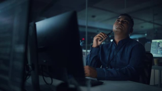夜间办公室: 在台式电脑上工作的英俊印度男子的肖像。数字企业家打字，创建软件，电子商务应用程序设计，