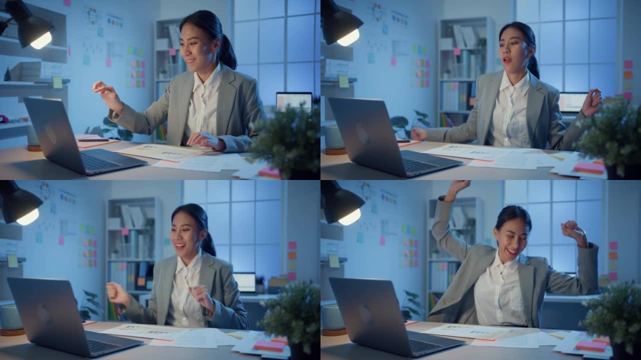 年轻的亚洲开朗的女商人坐在桌子上，用笔记本电脑检查最终报告并发送电子邮件，然后在晚上回到办公室之前享