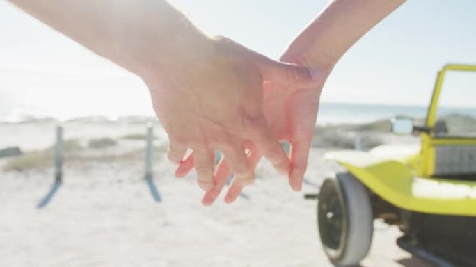 白人夫妇手牵着手站在海边的海滩越野车附近