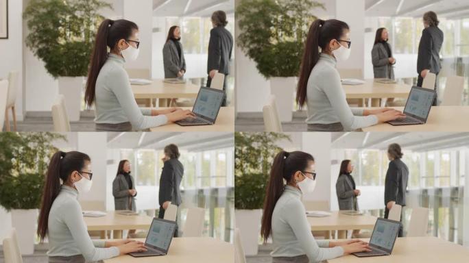 戴着面具的商务女士在笔记本电脑上工作