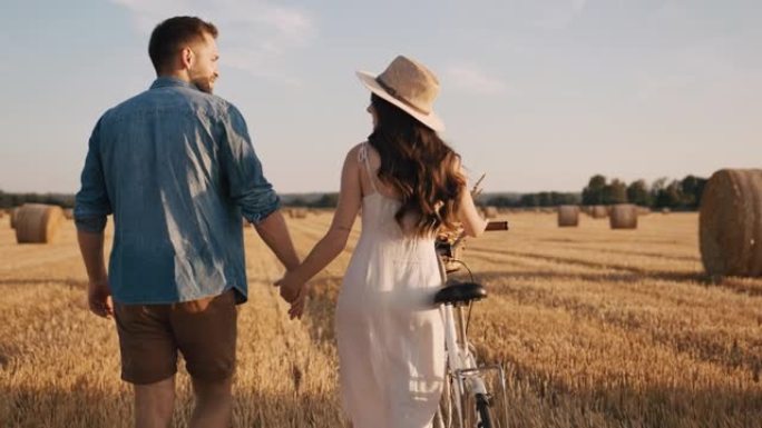 追踪，慢动作镜头的一对成年夫妇牵着手走在收获的田地上，在阳光明媚的日子里骑自行车