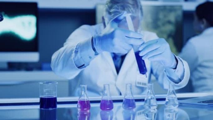 成熟的实验室科学家使用注射器和烧杯在紫外线照明的实验室中测试和检查化学反应。生物化学家和基因工程师在