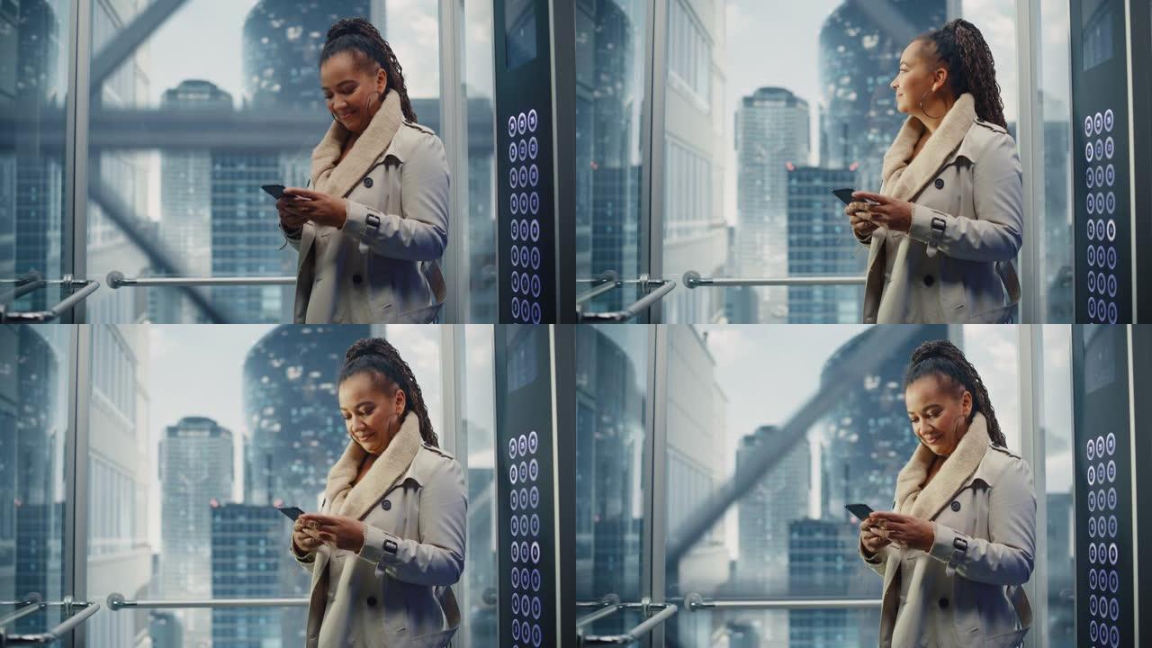 成功的黑人成年女性乘坐玻璃电梯到现代商务中心的办公室。美丽的非洲裔美国经理使用智能手机，写信息，查看