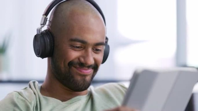 一个英俊的年轻人独自坐在家里并戴着耳机使用数字平板电脑的4k视频片段