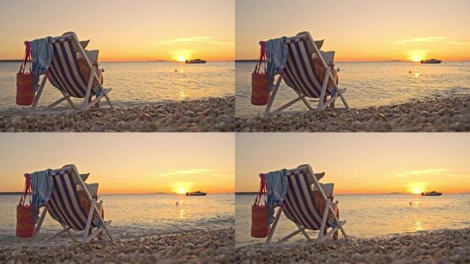 日落时，SLO MO女人在海滩上的椅子上看书